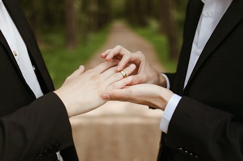 A picture of two male handing putting a wedding ring on